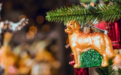 Een kerstornament in de vorm van een golden retriever hangt aan een tak van een kerstboom