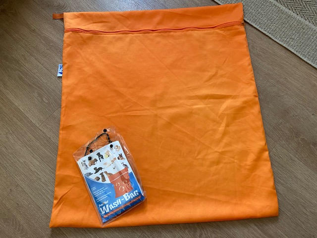Oranje waszak met rits ligt op de grond, met de verpakking er bovenop